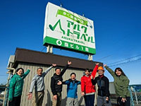 歩く旅専門店アルクトラベルの看板を指さす7人の男女