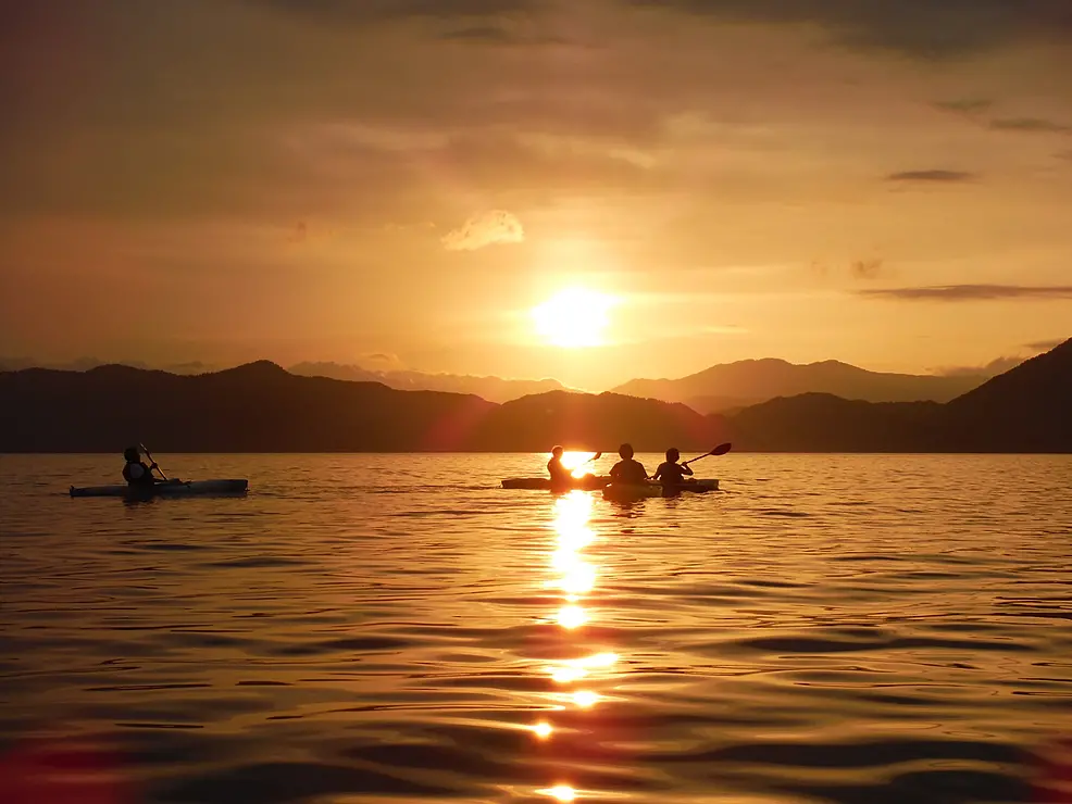 夕焼けに染まる湖でカヤックをする人たち
