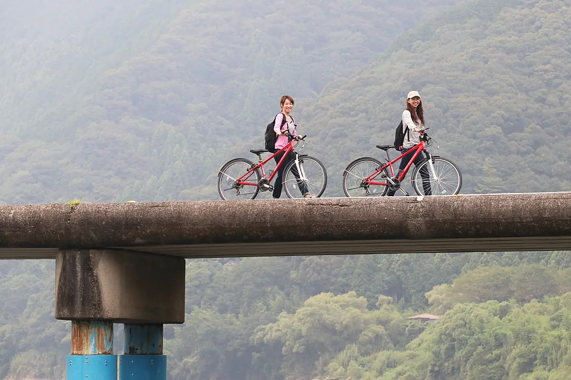 沈下橋の上を若い女性が2人自転車を押しながら歩いている