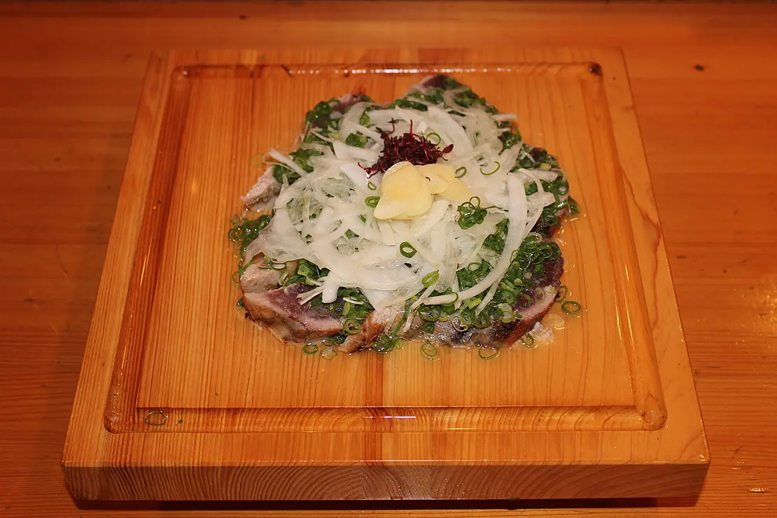 かつおの塩たたきの上にたっぷりスイラスされた玉ねぎとネギがかかっている