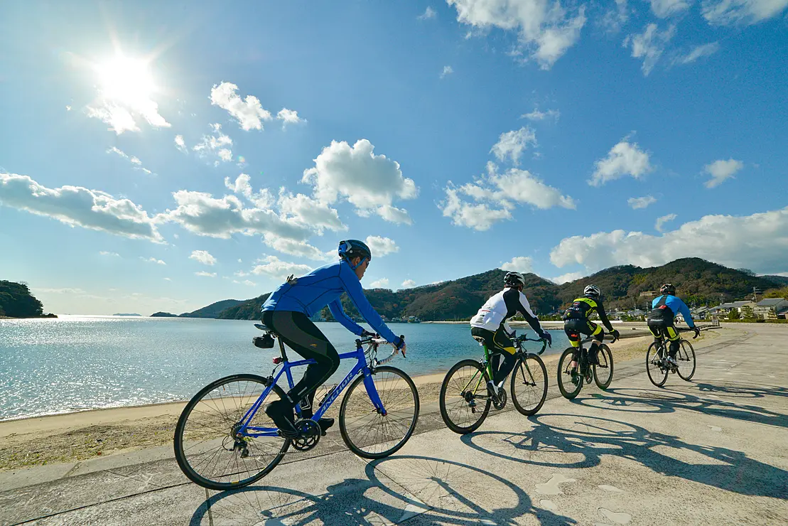 青空の下、海沿いの道で自転車に乗る人たち