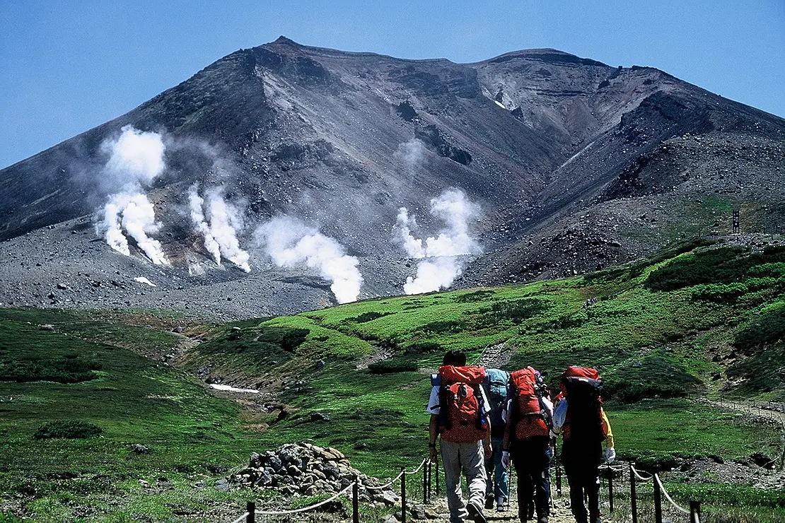 噴煙の上がる山に登る人々