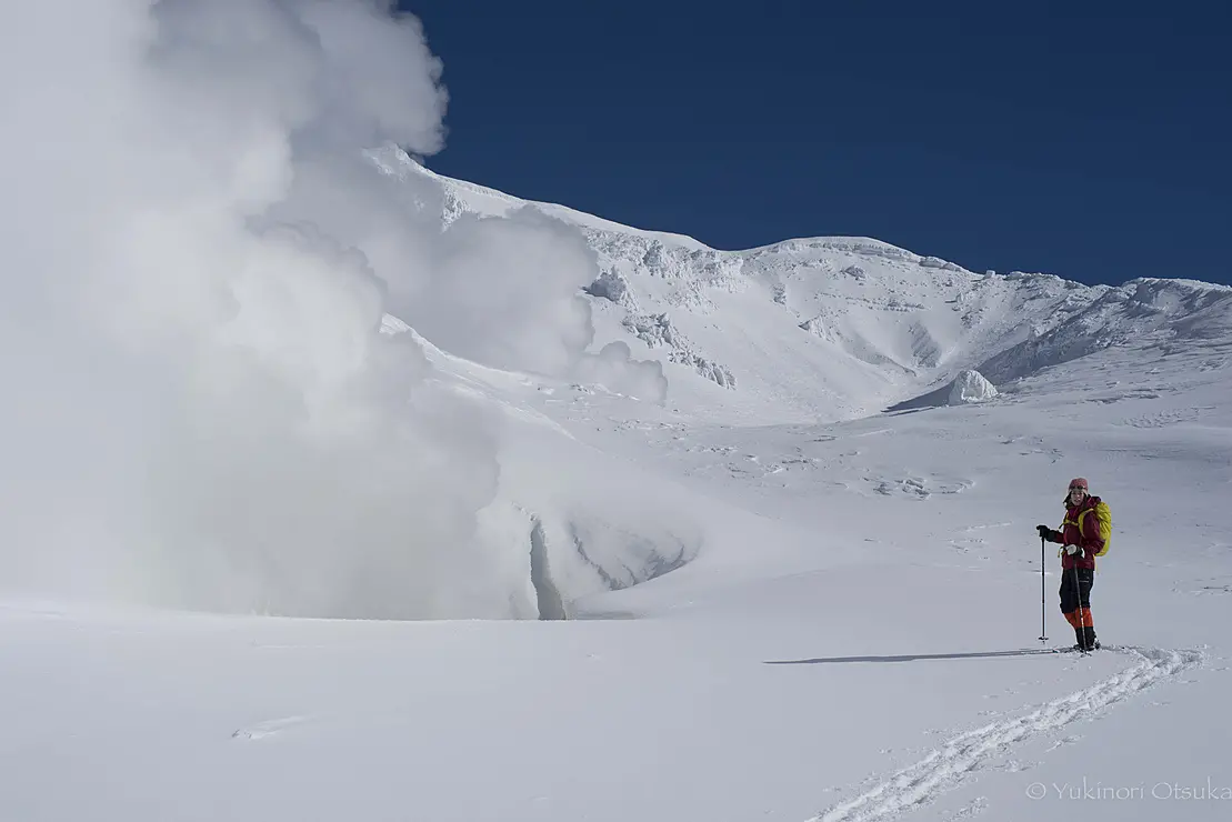 噴煙が出る雪山に佇む人