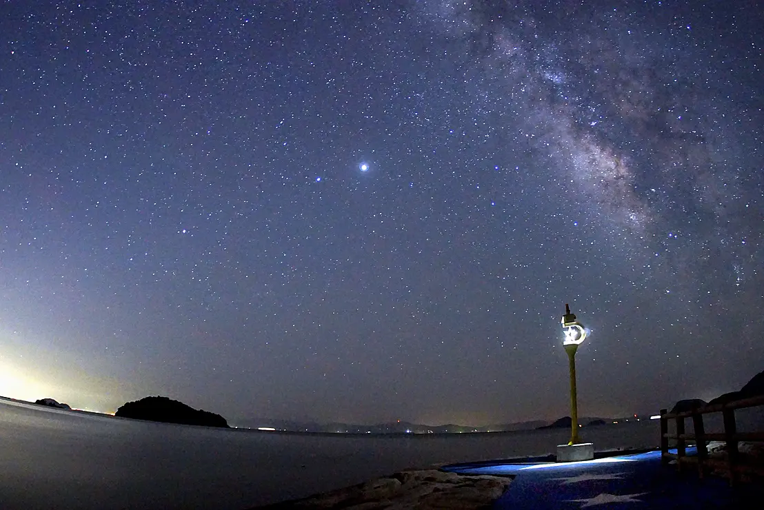 満点の星空の下に灯台が光っている