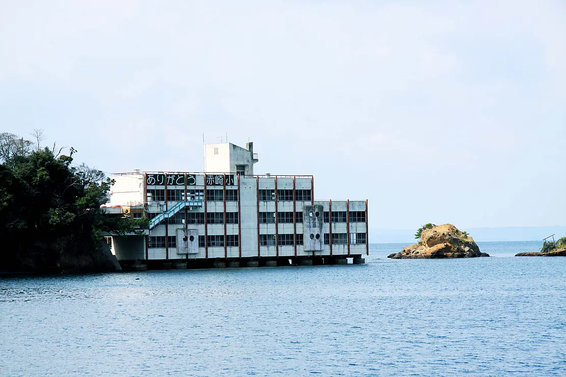 海辺に建つ白い校舎の旧赤崎小学校。周囲には小さな島々が浮かぶ静かな入り江が広がっている。