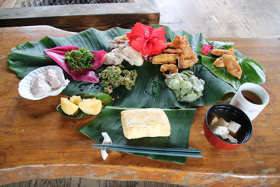バナナの葉の上に並べられた、薄焼き卵でおにぎりを包んだ卵おにぎりとたくさんのおかず