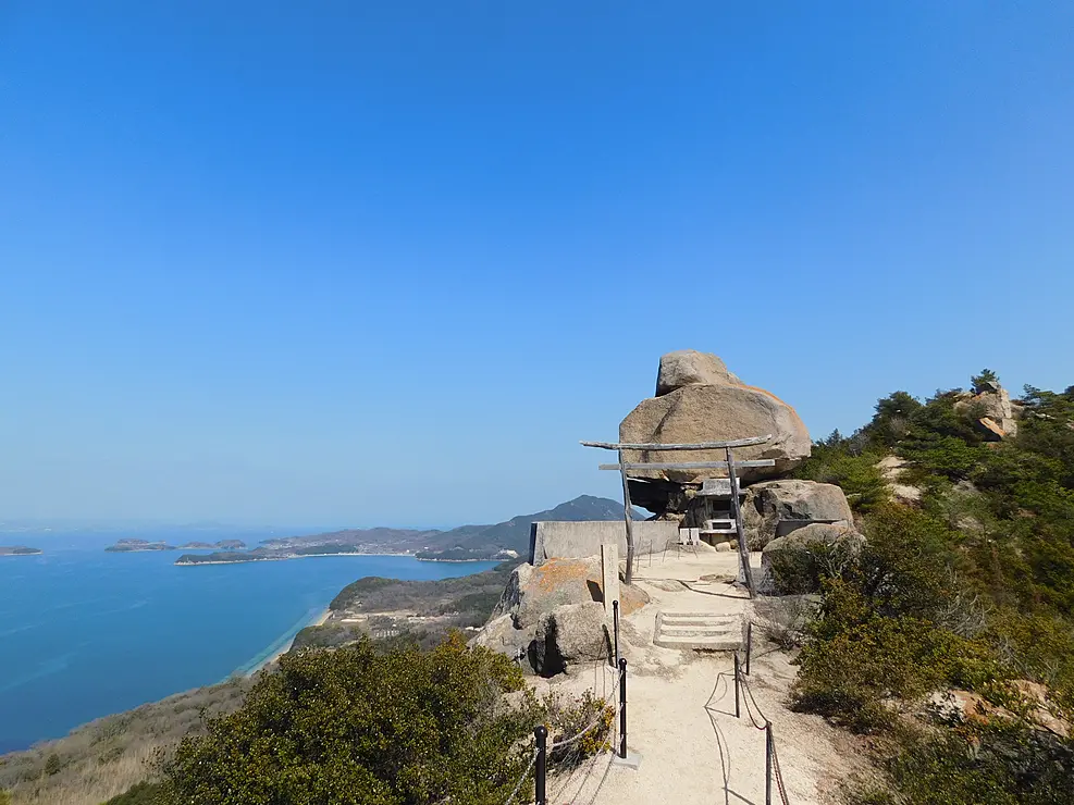 青空のなか崖の淵に大きな岩が建っている