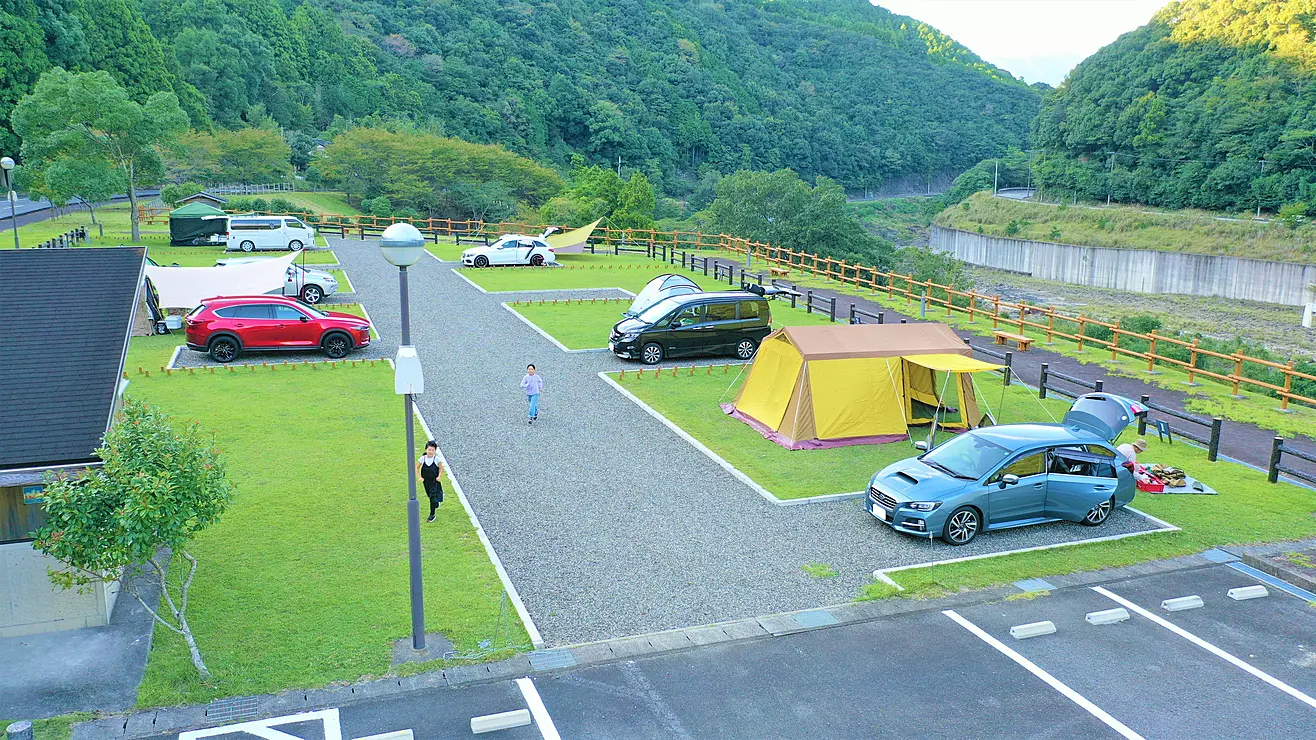 山に囲まれた川沿いのオートキャンプ場に車が数台止まっており、横にはテントが張られている