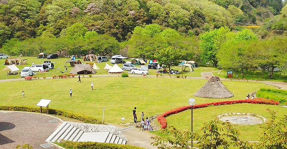 縄文時代の遺跡の遺構を残した芝生の公園でキャンプを楽しむ人々