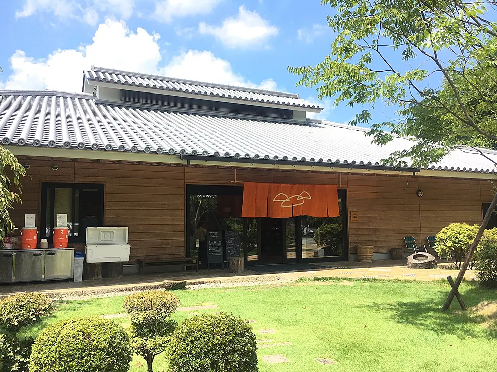 瓦屋根と板壁の日本家屋風の建物　入り口にはオレンジ色の暖簾が掛かっている