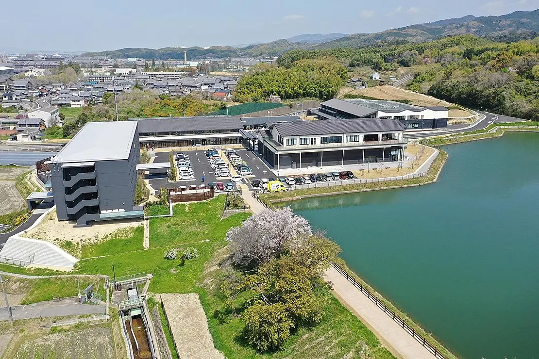 施設全景（空撮）右手には池、前には駐車場と緑の芝生が広がる。