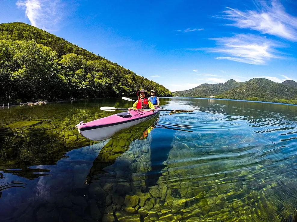 透き通った湖の中を赤いカヤックで進む人たち