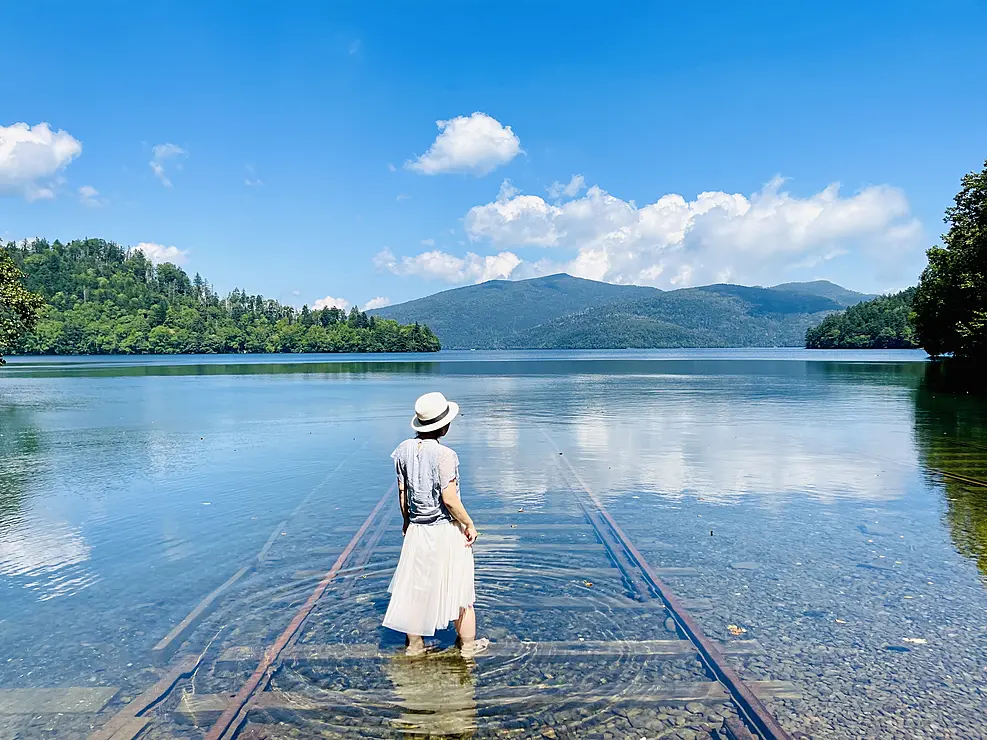 湖にある線路に立つ白い服の女の人