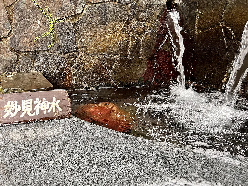 岩の間から水が流れ落ちる湧水（妙見神水）の風景