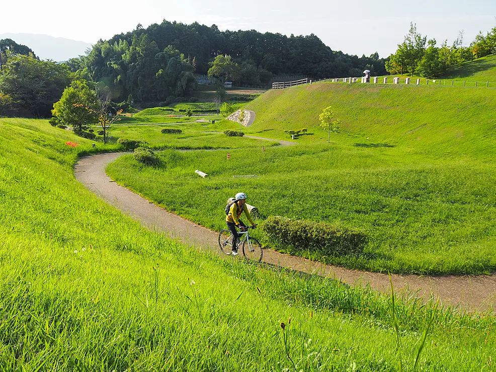 古墳を覆う青々とした芝生の間の小路を自転車で駆け抜ける人