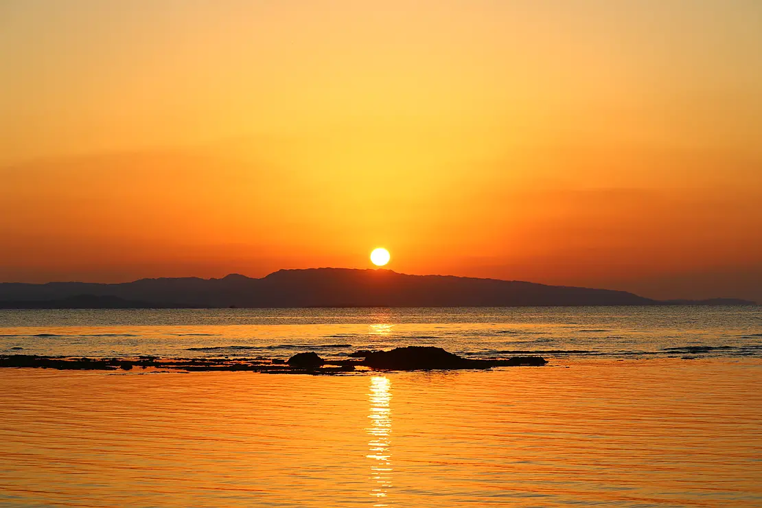 水平線の向こうに夕日が沈み、周囲が橙色に染まる