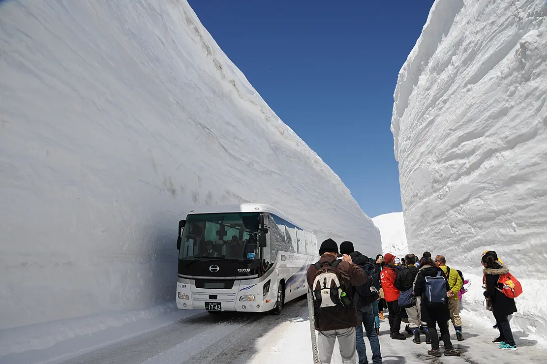雪の壁に囲まれた道を走る大型バス