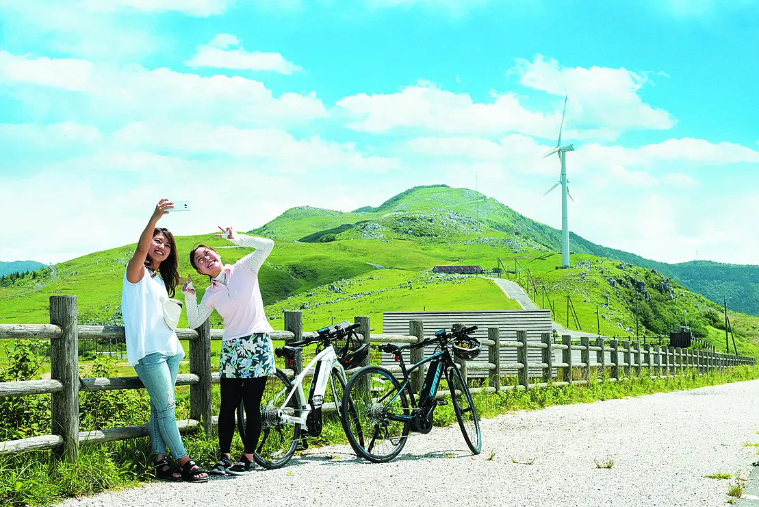 青空の下、若い女性が四国カルスト台地を背景に写真を撮影している