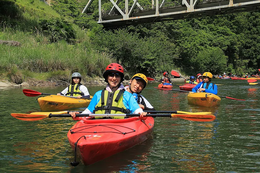 緑豊かな木々に囲まれた穏やかな川面でカヌーを楽しむ人々