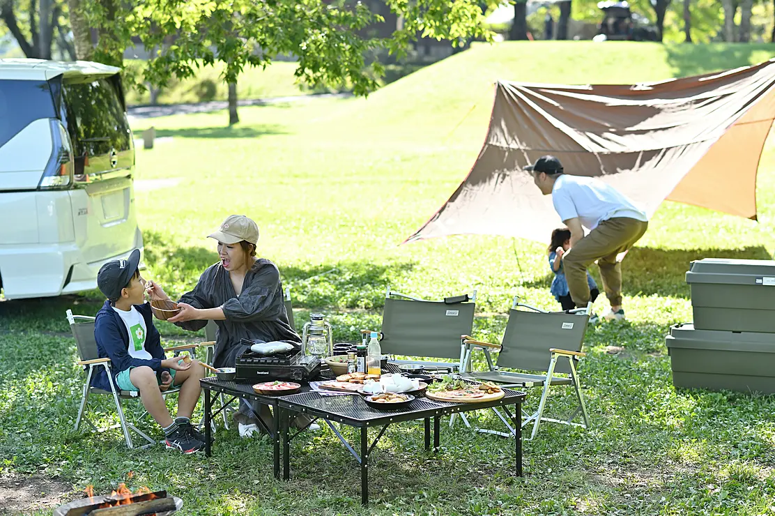 キャンプ場に爽やかな風が吹くなかテーブルを囲んでくつろぐ親子