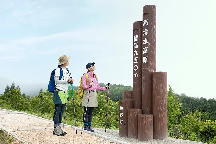 頂上看板と青いザックの女性と黄色いザックの女性