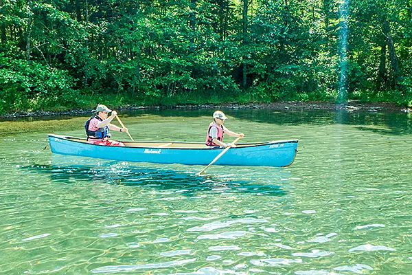 透明な水面を青いカヌーで進む二人