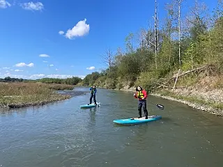 ライフジャケットを着た2人が川でパドルボードを楽しんでいる様子