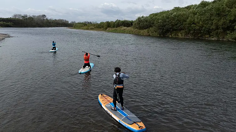 ライフジャケットを着た3人が川でパドルボードを楽しんでいる様子