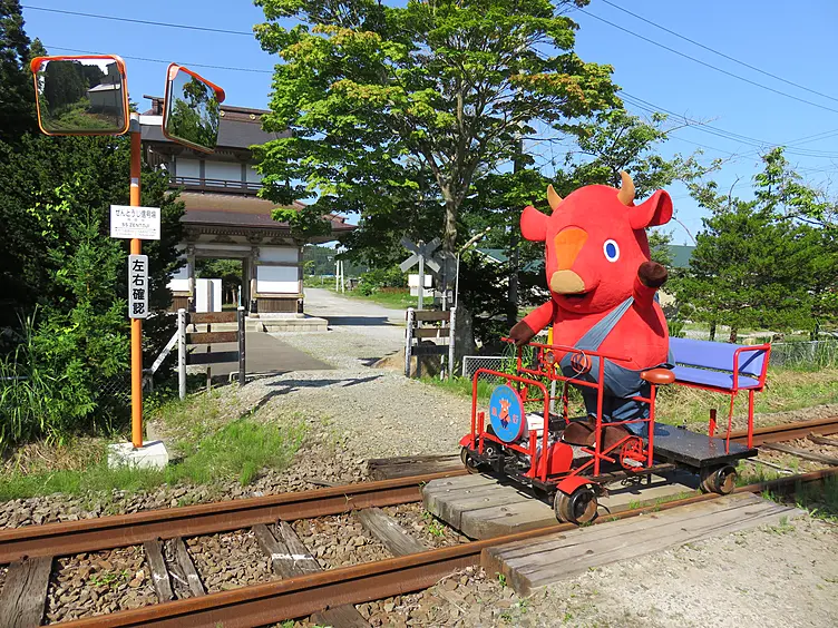 赤い牛のきーこ君がペダル付きのトロッコに乗る様子