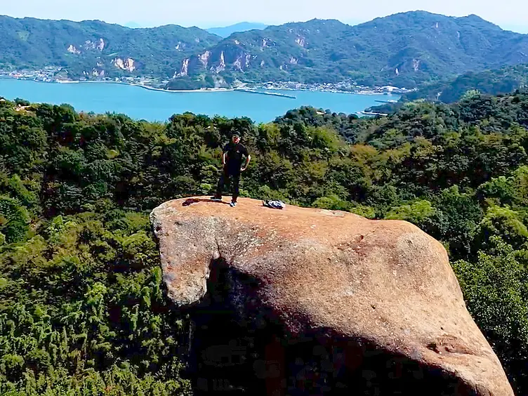 海と島を背景に大玉岩の上に男性が立っている