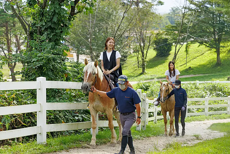 女性2人が楽しそうに男性に馬を引いてもらいながら乗馬している