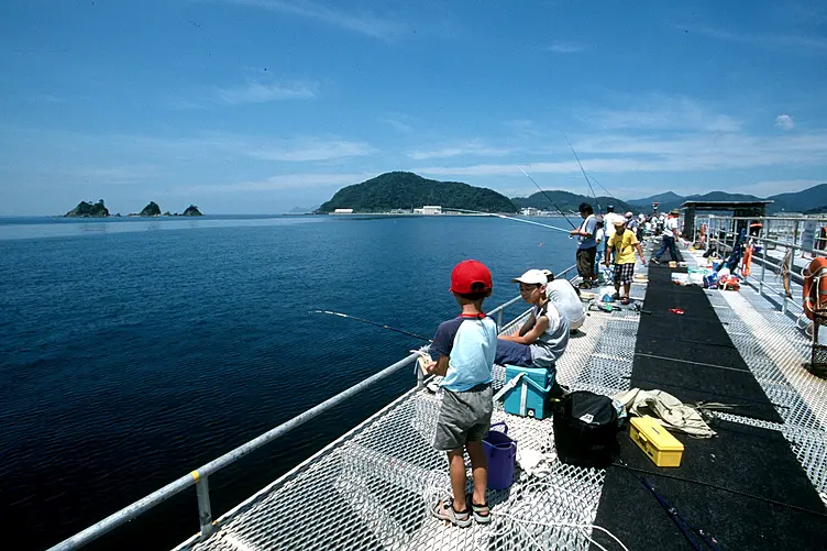 青い海と島が見える釣り場で子供たちが楽しそうに釣りをしている