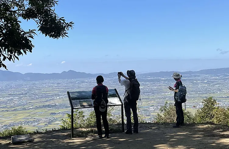 山頂の看板の前で奈良盆地を見渡す人々