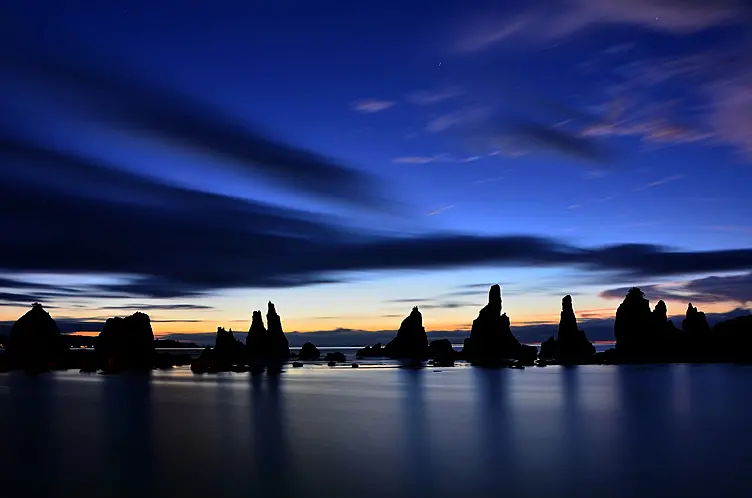 夕暮れの空を背景に海中から一列に突き出した岩柱