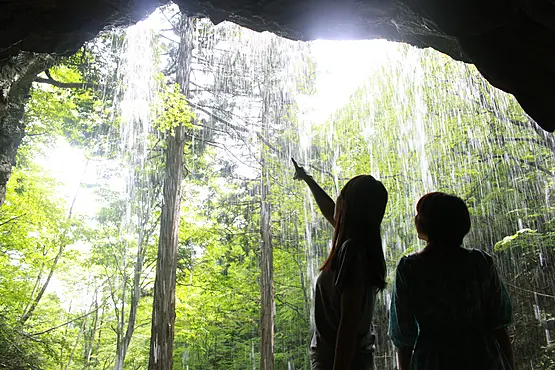 滝の裏側から流れ落ちる清水を眺める２人の女性