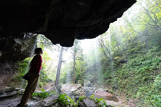 滝の裏側から流れ落ちる清水を眺める1人の女性